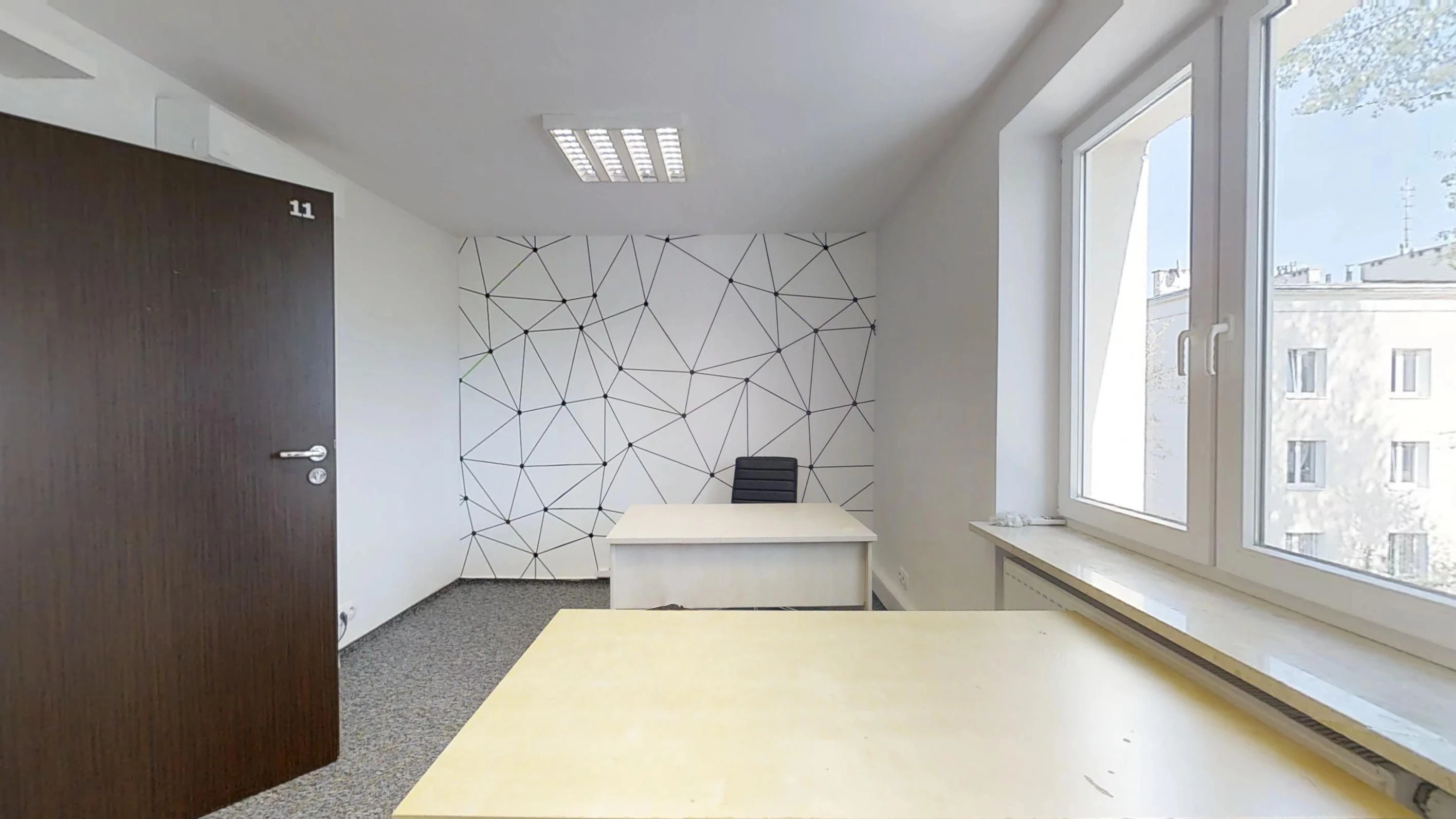 Dwa jasne biurka, geometryczny mural na tylnej ścianie i duże okno po prawej stronie biura
